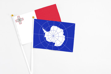 Antarctica and Malta stick flags on white background. High quality fabric, miniature national flag. Peaceful global concept.White floor for copy space.