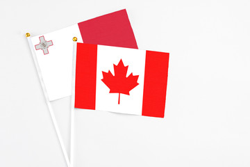 Canada and Malta stick flags on white background. High quality fabric, miniature national flag. Peaceful global concept.White floor for copy space.