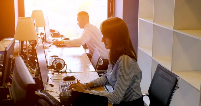 the girl and the guy work in the office at the computers. their desks are near the window and sunlight shines into the office. proress 422 25p. slow motion