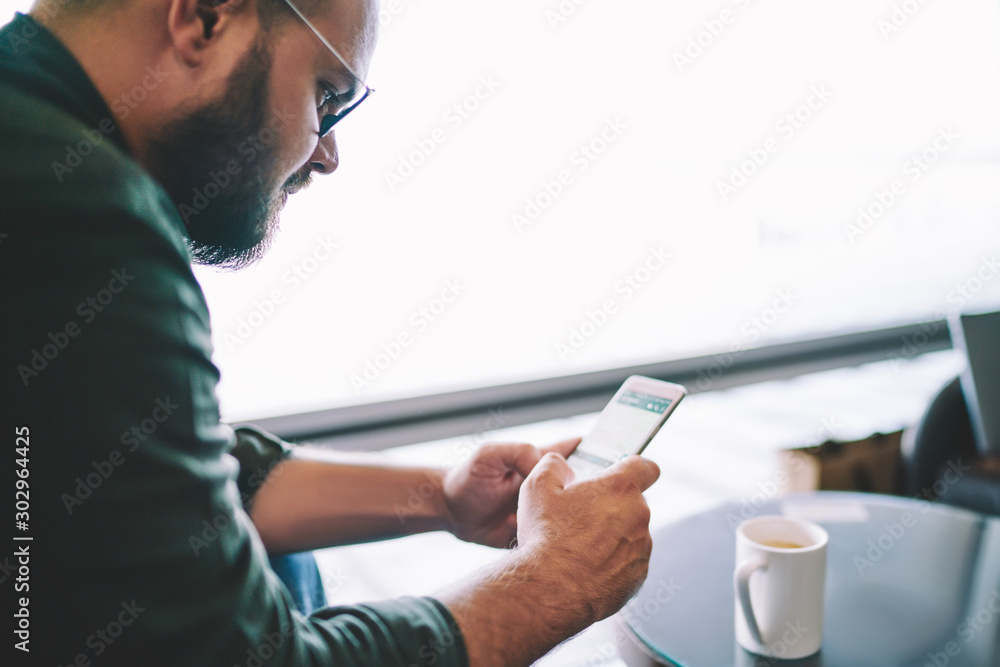 Poster cropped image of pensive bearded man in eyewear making peyment online via free high speed internet c
