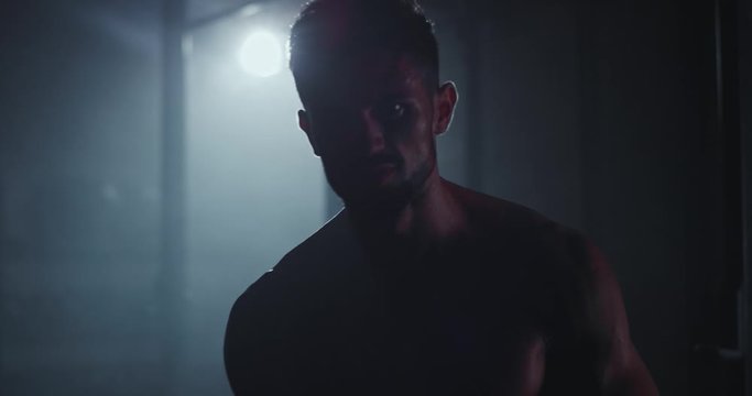 Attractive bodybuilding guy walking straight to the camera in a dark cross fitness class