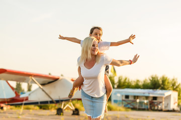 field with plane flying over it, mother and daughter near airplane