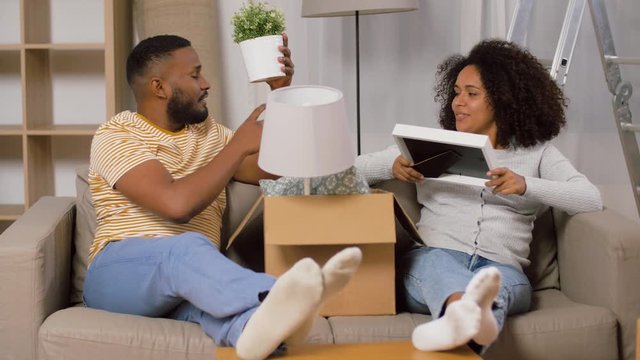 moving, people, repair and real estate concept - happy african american couple with photo frame and cardboard boxes sitting on sofa at new home