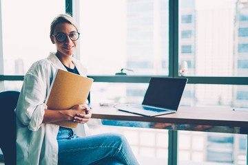 Half length portrait of successful businesswoman with folder of documents in hands smiling at...