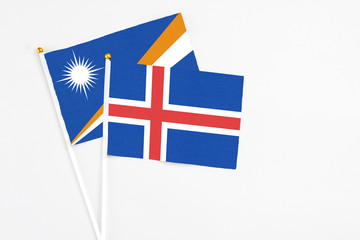 Fototapeta premium Iceland and Marshall Islands stick flags on white background. High quality fabric, miniature national flag. Peaceful global concept.White floor for copy space.