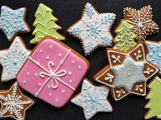Fototapeta na wymiar Homemade gingersnaps coverd icing on the dark plate: gift; pine-trees; snowflakes and sters; delicious cookies with Christmas shapes
