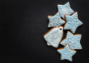 Homemade gingersnaps coverd icing on the dark plate: иудд and stars; delicious cookies with Christmas shapes