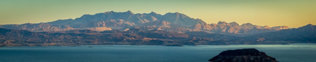 Morning light over Lake Meade with an island in the foreground and a mountain in that background.