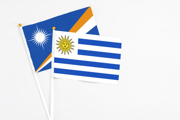 Uruguay and Marshall Islands stick flags on white background. High quality fabric, miniature national flag. Peaceful global concept.White floor for copy space.