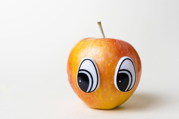 Red apple with eyes looking to the side. Funny cute picture of fruits. Light background, place for...