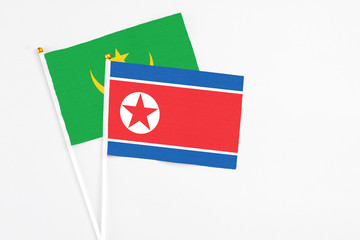 North Korea and Mauritania stick flags on white background. High quality fabric, miniature national flag. Peaceful global concept.White floor for copy space.