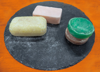 handmade soaps with different aromas and bright colors, displayed on a black slate disc
