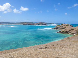 An areal view on idyllic Tanjung Aan beach in Lombok, Indonesia. The bay of water is guarded by a headland. Water has many shades of blue. Perfect day for relaxation on the beach.