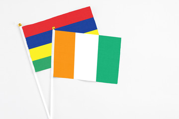 Cote D'Ivoire and Mauritius stick flags on white background. High quality fabric, miniature national flag. Peaceful global concept.White floor for copy space.