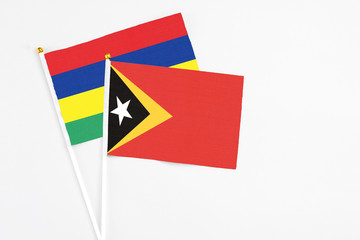 East Timor and Mauritius stick flags on white background. High quality fabric, miniature national flag. Peaceful global concept.White floor for copy space.