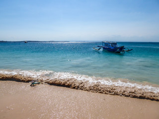 A view on a bay on Pink Beach, Lombok Indonesia. A few colourful boats anchored to the shore. The water has many shades of blue. The heavenly beach is surrounded by small hills. Paradise beach.