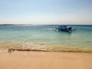 A view on a bay on Pink Beach, Lombok Indonesia. A few colourful boats anchored to the shore. The water has many shades of blue. The heavenly beach is surrounded by small hills. Paradise beach.