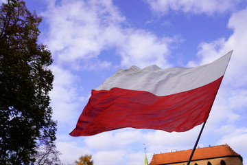 Polish red and white flags in the Old town in front of the building on a Sunny day.May 1, November 11, flag, independence or labor Day.Public holiday in Poland.flag on blue sky background with clouds
