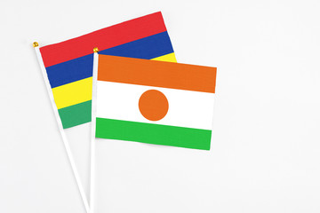 Niger and Mauritius stick flags on white background. High quality fabric, miniature national flag. Peaceful global concept.White floor for copy space.