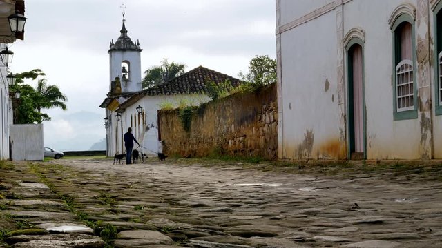 Woman walking dog on a cobblestone street in rural neighbourhood in Brazil, Static
