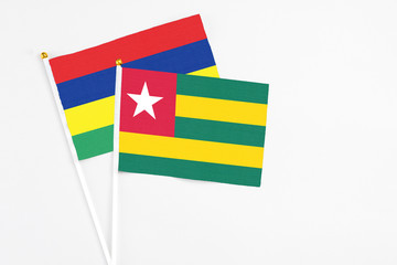 Togo and Mauritius stick flags on white background. High quality fabric, miniature national flag. Peaceful global concept.White floor for copy space.