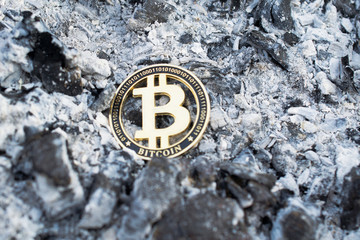Cryptocurrency bitcoin token among ashes. Loss of capital. Close up.