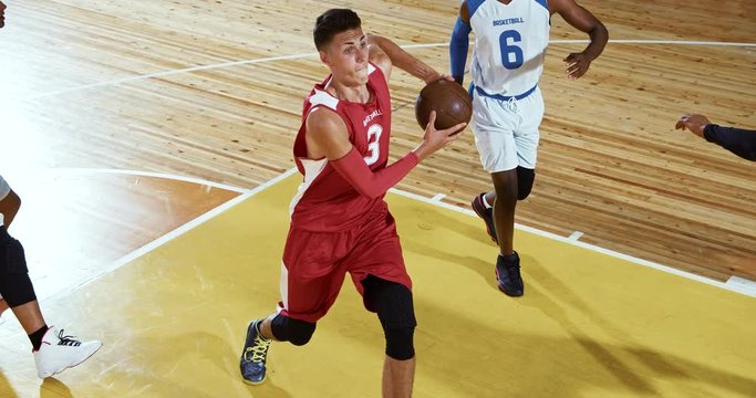 Professional basketball player in action performing slam dunk in a basketball hoop on a sports arena.