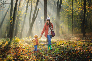 A young mother with a toddler daughter walking in forest in autumn nature.