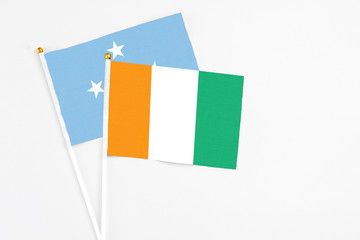 Cote D'Ivoire and Micronesia stick flags on white background. High quality fabric, miniature national flag. Peaceful global concept.White floor for copy space.