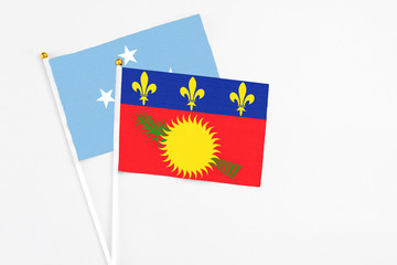 Guadeloupe and Micronesia stick flags on white background. High quality fabric, miniature national flag. Peaceful global concept.White floor for copy space.