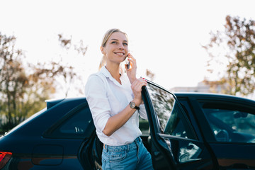 Smiling woman with smartphone getting out of car