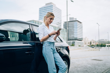 Concentrated woman with smartphone leaning against car