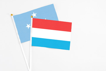 Luxembourg and Micronesia stick flags on white background. High quality fabric, miniature national flag. Peaceful global concept.White floor for copy space.