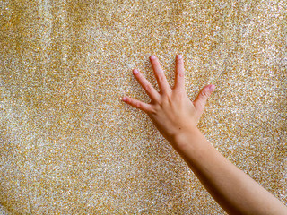 Child's hand touches on glitter gold fabric background