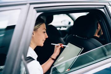 Cheerful lady with tablet sitting in car back seat