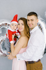 Obraz premium Happy beautiful young family with baby in little Santa costume smile and celebrate new year 2020