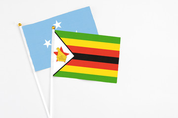 Zimbabwe and Micronesia stick flags on white background. High quality fabric, miniature national flag. Peaceful global concept.White floor for copy space.