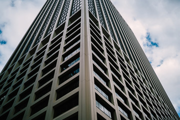 Fototapeta premium Perspective view of tall concrete skyscraper with windows on exterior rising up in sky, geometric corporate building with offices and luxury apartments for rent in business center of megalopolis.