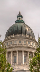Fototapeta na wymiar Vertical frame Famous Utah State Capitol Building dome framed with trees against cloudy sky