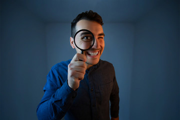 Shocked man with magnifying glass on grey background. Curious young man with magnifying glass Isolated on grey background.