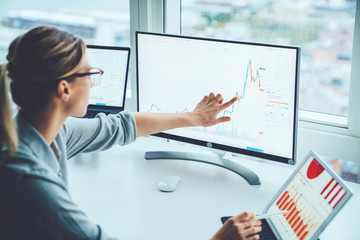 Business woman study financial market to calculate possible risks and profits.Female economist accounting money with statistics graphs pointing on screen of computer at desktop. Quotations on exchange - obrazy, fototapety, plakaty