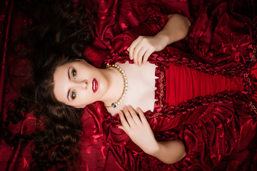 A beautiful young girl lies on a magnificent red dress of the Rococo era.