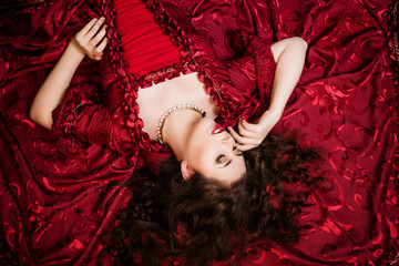 A beautiful young girl lies on a magnificent red dress of the Rococo era.
