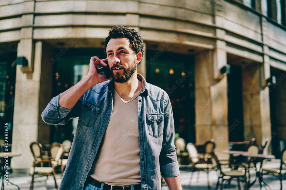 Poster stylish bearded hipster guy dressed in branded denim wear looking away while calling on smartphone d