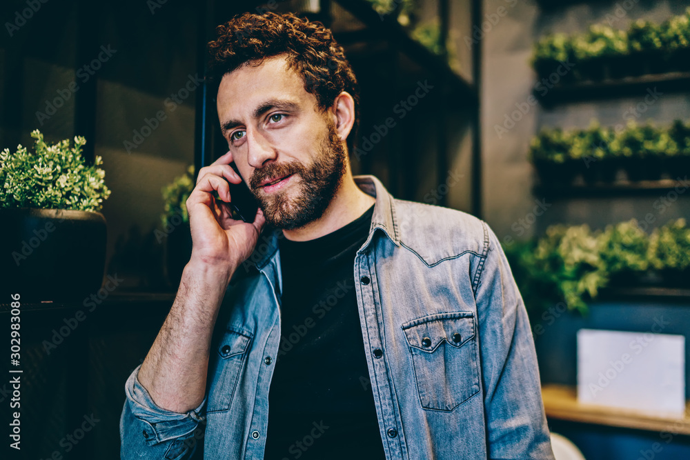 Poster bearded young man dressed in casual wear calling on smartphone and talking with mobile operator abou
