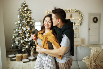 happy couple in love in the morning near the Christmas tree, a guy hugs a girl, morning Christmas. hearth, home clothes and sweaters.