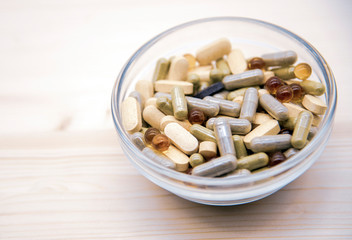 Fototapeta na wymiar Glass bowl with lots of pills and capsules on a wooden background.