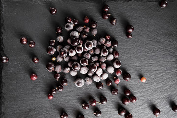 frozen blackcurrant berries covered with hoarfrost scattered on a slate dish.