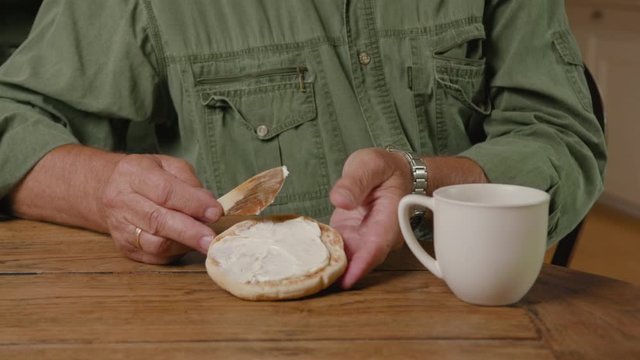 Old married man/farmer making a sandwich with butter and ham for breakfast. Organic colours and clothing with greenery. Coffee cup in Swedish cottage near the fireplace.