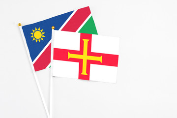 Fototapeta premium Guernsey and Namibia stick flags on white background. High quality fabric, miniature national flag. Peaceful global concept.White floor for copy space.